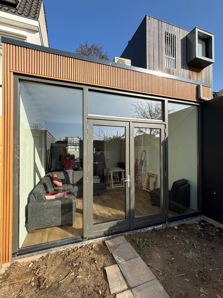 Moderne aanbouw met verticale houten gevelbekleding, donkere kozijnen en dubbele tuindeuren in Utrecht Leidsche Rijn